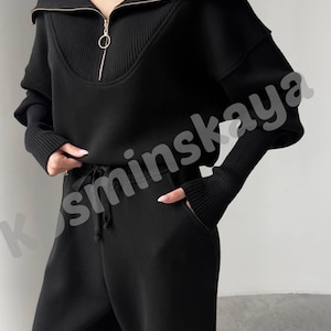 May include: Black two-piece outfit featuring a zip-up sweater and matching pants. The sweater has a ribbed collar and cuffs, with a gold zipper. The pants have a drawstring waist and pockets. The outfit is made of a soft, comfortable material.