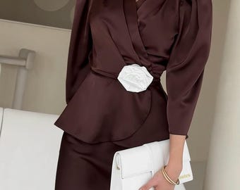 May include: A brown satin ensemble featuring a wrap top with a white floral accent at the waist and a matching skirt. The outfit is paired with a white clutch and gold bracelet. The text "ElenaKosminskaya" is visible.