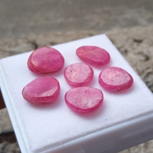 Può includere: Sei pietre preziose di rubino rosa di varie forme e dimensioni, esposte su una superficie bianca.