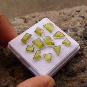 以下が含まれることがあります： 白い箱に、様々な形と大きさの緑色の宝石が12個並んでいます