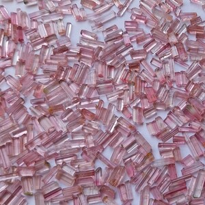 May include: A collection of pink and green tourmaline crystals, also known as rubellite, in various sizes and shapes. The crystals are translucent and have a natural, raw appearance.