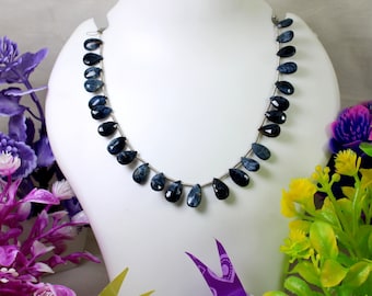 May include: A strand of dark blue gemstone beads in a teardrop shape, strung on a silver wire, displayed on a white mannequin bust.