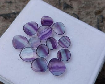 May include: A collection of 12 purple and white fluorite gemstones, each with a unique pattern of stripes and swirls. The stones are smooth and polished, and they have a slightly iridescent sheen.