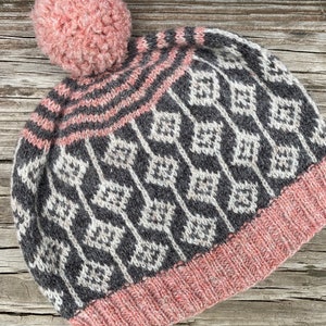 May include: A knitted hat with a pink pom pom and a geometric pattern in shades of grey and white. The hat has a pink brim.