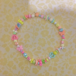 May include: A colorful beaded necklace with various shapes, including hearts, stars, butterflies, and flowers. The beads are in shades of pink, blue, green, yellow, and white.