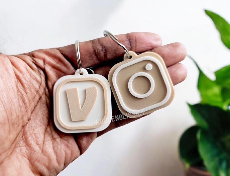 Pu&ograve; includere: Due portachiavi, uno con una lettera V bianca e l'altro con un logo Instagram marrone, entrambi con contorni bianchi.