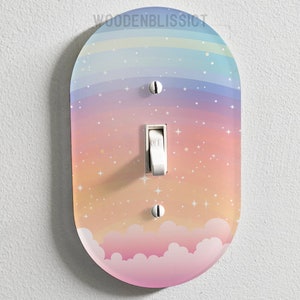 Könnte beinhalten: Ein Lichtschalter-Abdeckung mit einem pastellfarbenen Regenbogen-, Wolken- und Sternen-Design. Die Abdeckung ist aus Kunststoff und hat eine glänzende Oberfläche.