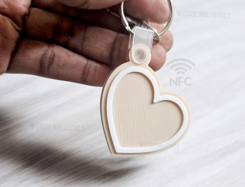 Pu&ograve; includere: Un portachiavi a forma di cuore beige con un contorno bianco e un anello argentato. Il portachiavi ha un chip NFC e il testo "NFC" &egrave; stampato sul retro.