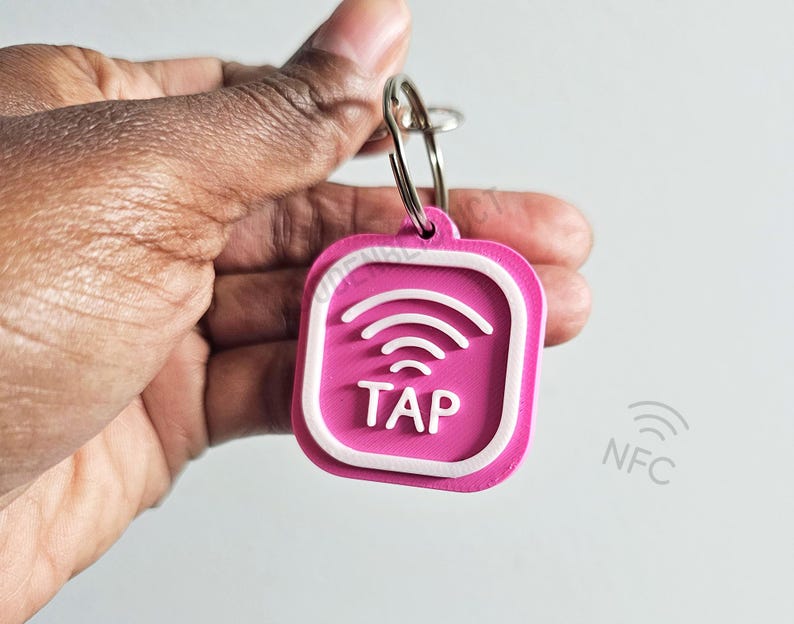 Pu&ograve; includere: Un portachiavi rosa con un bordo bianco e un simbolo wireless bianco con la parola "TAP" in lettere bianche. Il portachiavi ha un anello argentato.