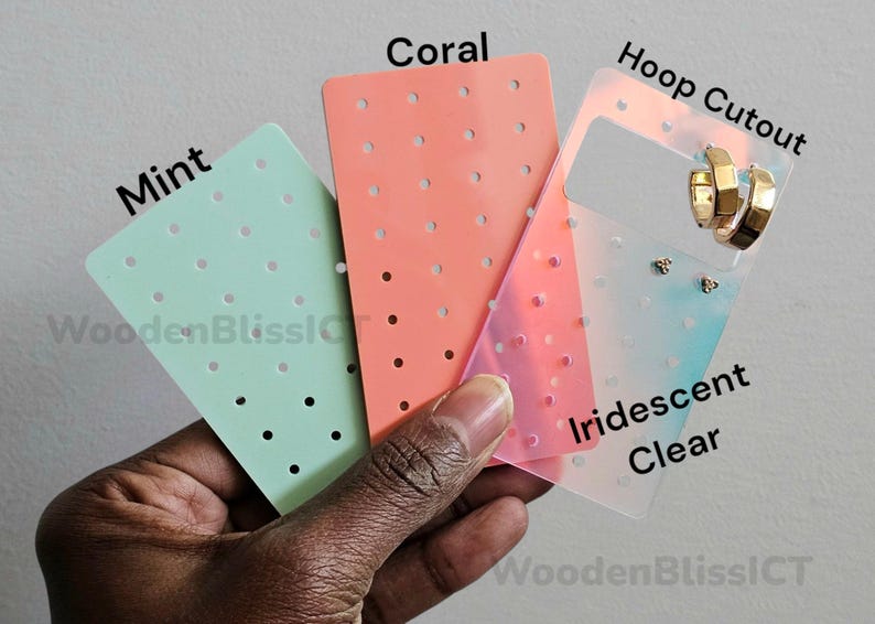 May include: Three earring display cards in mint green, coral, and iridescent clear. The iridescent card has a cutout for hoop earrings. The text "Hoop Cutout" is printed on the card. The text "Iridescent Clear" is printed on the card. The text "Coral" is printed on the card. The text "Mint" is printed on the card.