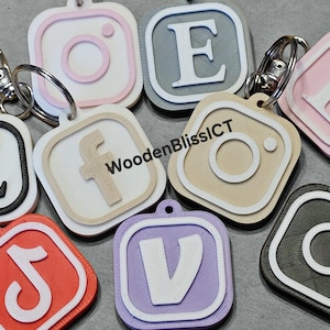 Pu&ograve; includere: Un set di nove portachiavi con diversi loghi di social media e lettere. I portachiavi sono realizzati in diversi colori, tra cui rosa, grigio, beige, nero, bianco, rosso e viola. I portachiavi sono di forma quadrata con angoli arrotondati e hanno un bordo bianco attorno al logo o alla lettera. I portachiavi sono attaccati a anelli portachiavi argentati. Il testo "WoodenBlissICT" &egrave; visibile su uno dei portachiavi.