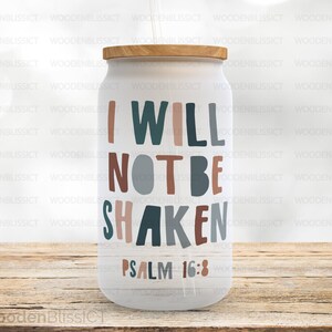 Puede incluir: Un vaso blanco con tapa de madera y un diseño marrón, azul y gris que dice "No seré sacudido Salmo 16:8".