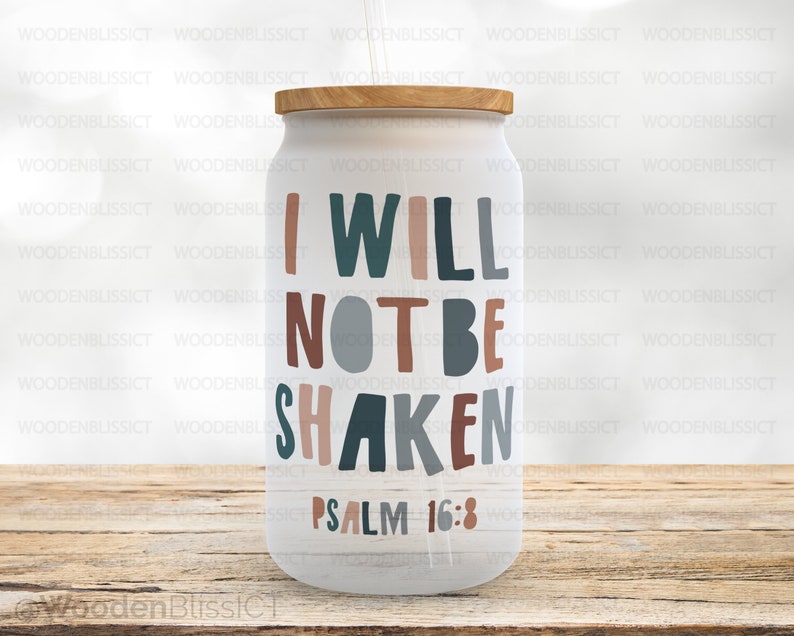 Puede incluir: Un vaso blanco con tapa de madera y un dise&ntilde;o marr&oacute;n, azul y gris que dice "No ser&eacute; sacudido Salmo 16:8".