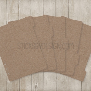 May include: A stack of brown paper planner dividers with pre-punched holes and tabs. The text "STICKSBYDESIGN.COM" is printed on the dividers. The dividers are arranged on a light wood grain surface.