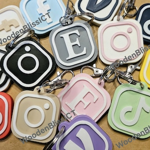 Pu&ograve; includere: Una collezione di portachiavi quadrati e colorati con vari loghi e lettere. I portachiavi sono in plastica e hanno un bordo bianco. I loghi includono Instagram, TikTok, Facebook e la lettera E. I portachiavi sono attaccati a anelli portachiavi argentati.