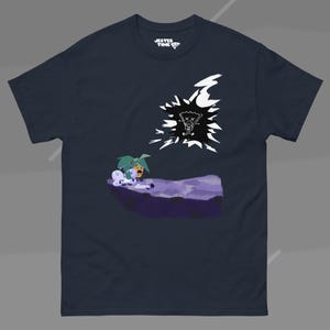 Può includere: Una t-shirt a maniche corte blu navy scuro con una stampa grafica raffigurante un paesaggio viola con due piccoli personaggi e una forma bianca frastagliata contenente un'icona nera con occhi sbarrati. L'etichetta interna riporta JESTER TIME.