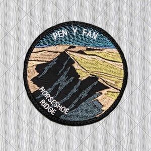 Op de afbeelding: Een ronde geborduurde patch met een landschapsscène met een donkere bergtop, beige hellingen en een blauwe lucht. De tekst "PEN Y FAN" is in het wit bovenaan geborduurd en "HORSESHOE RIDGE" staat in het wit linksonder.