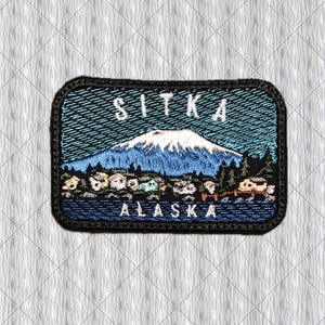 Op de afbeelding: Een rechthoekige geborduurde patch met een landschap met een besneeuwde berg, een bos en een klein stadje. De tekst SITKA is in het wit bovenaan geborduurd en ALASKA is in het wit onderaan geborduurd op een blauwe achtergrond.