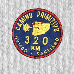 Può includere: Toppa ricamata circolare con sfondo blu e bordo rosso. La toppa presenta il testo "CAMINO PRIMITIVO OVIEDO SANTIAGO" in giallo, insieme al numero "320 km" e un disegno di conchiglia e mappa gialla.