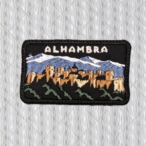 Könnte beinhalten: Ein rechteckiger bestickter Aufnäher mit schwarzem Rand und dem Wort ALHAMBRA in weißen Großbuchstaben. Das Design zeigt eine beigefarbene Festungsanlage vor blauen Bergen mit schneebedeckten Gipfeln und grüner Vegetation im unteren Bereich.
