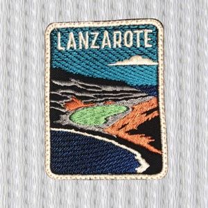 Puede incluir: Parche bordado con la palabra "LANZAROTE" en blanco sobre fondo azul. El parche representa un paisaje con una zona verde, terreno naranja y negro, y un cielo azul con una nube blanca. Tiene un borde beige.