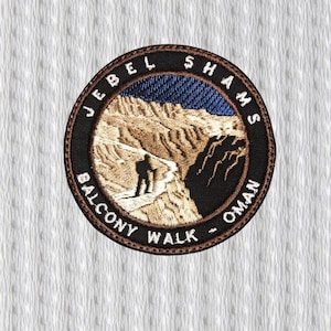 Peut inclure: Écusson brodé circulaire avec un paysage de montagne et une personne en randonnée. Le texte "JEBEL SHAMS BALCONY WALK - OMAN" est disposé en cercle. Les couleurs sont marron, beige, bleu et noir. Idéal pour un sac à dos ou une veste.