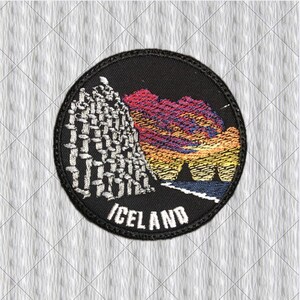 May include: A circular embroidered patch with a black background featuring a white basalt column formation on the left, a colourful sunset sky in shades of pink, orange, and yellow, and the word ICELAND stitched in white capital letters at the bottom.