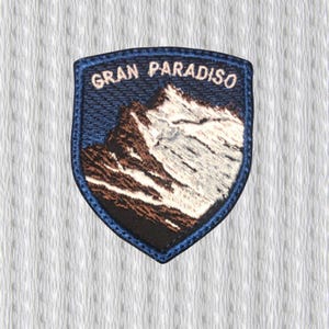 May include: Embroidered patch with the text "GRAN PARADISO" above a mountain range. The patch has a blue border and features a mountain scene with brown and white details against a dark blue sky.