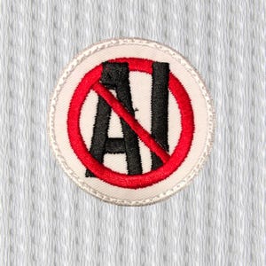Op de afbeelding: Geborduurde ronde patch met een witte achtergrond en een rode cirkel met een streep erdoor. Binnen de cirkel staan de zwarte letters "AI", ook doorgestreept met een rode lijn. De patch heeft een witte rand.