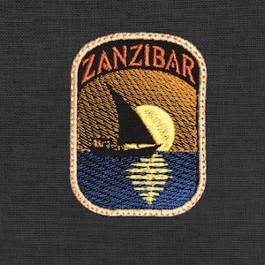 Op de afbeelding: Geborduurde patch met het woord "ZANZIBAR" in oranje boven een zonsondergangscène. Een zwarte zeilboot vaart op blauw water met de weerspiegeling van de zon. De patch heeft een beige rand en staat tegen een donkere achtergrond.