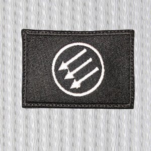 May include: Black rectangular patch with a white circle containing three downward-pointing arrows. The patch has a black border and is set against a textured white background.