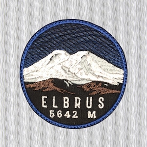 May include: Embroidered patch featuring a mountain range with the text "ELBRUS" and "5642 M". The patch has a blue border, a dark blue sky, white mountain peaks, and brown terrain. The text is in white.