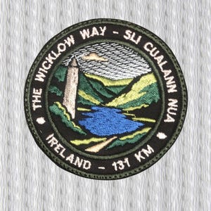 May include: Embroidered patch featuring a scenic landscape with a tower, lake, and mountains. The patch is circular with text that reads "THE WICKLOW WAY - SLI CUALANN NUA IRELAND - 131 KM" in a dark green border.