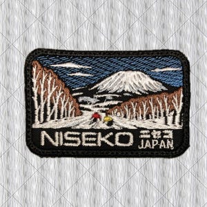 May include: A rectangular embroidered patch featuring a snowy mountain landscape with bare trees, two skiers in red and yellow jackets, and the text NISEKO JAPAN in white capital letters against a black background with a black stitched border.