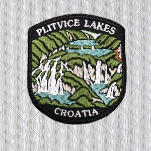 Può includere: Una toppa ricamata a forma di scudo che raffigura il paesaggio dei laghi di Plitvice in Croazia. Il design include colline verdi, acqua azzurra e cascate bianche. Il testo PLITVICE LAKES si trova in alto e CROATIA in basso sulla toppa.