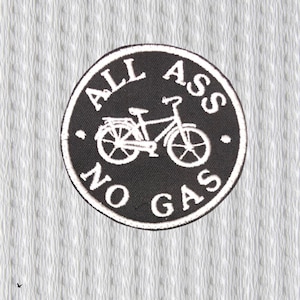 Può includere: Una toppa circolare in bianco e nero con la scritta "ALL ASS NO GAS" che circonda un'illustrazione di bicicletta. La toppa è su uno sfondo grigio chiaro strutturato.