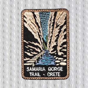 May include: Embroidered patch featuring a scenic view of a gorge with a river running through it. The patch has a black background with tan and blue details. Text at the bottom reads "SAMARIA GORGE TRAIL • CRETE". The patch has a brown border.