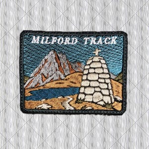 Könnte beinhalten: Gestickter Aufnäher mit einer Berglandschaft mit See und Steinstruktur. Der Aufnäher trägt den weißen Schriftzug "MILFORD TRACK". Das Design umfasst Blau-, Braun- und Weißtöne mit einem schwarzen Rand.