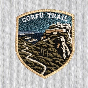May include: Embroidered patch with the text "CORFU TRAIL" at the top. The patch features a landscape scene with a winding path, mountains, and a blue sky. The patch has a gold border.