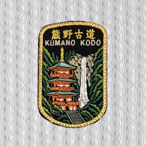 Puede incluir: Parche bordado con una pagoda japonesa, una cascada y follaje. El parche tiene el texto "KUMANO KODO" y caracteres japoneses. El parche es rectangular con un borde dorado, sobre un fondo blanco.