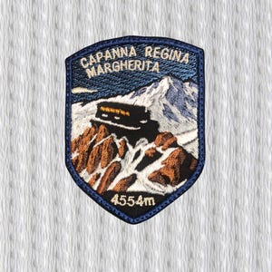 Può includere: Toppa ricamata raffigurante un paesaggio montano con la scritta "CAPANNA REGINA MARGHERITA" e "4554m". Il disegno comprende un edificio su uno sperone roccioso, montagne innevate e un bordo blu scuro.