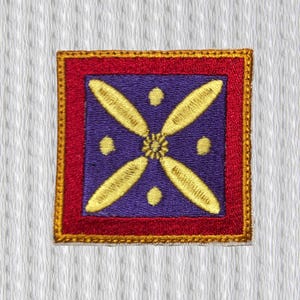May include: Square embroidered patch with a purple centre featuring a gold floral design and gold dots. The patch has a red border with a gold stitched edge, set against a white textured background.