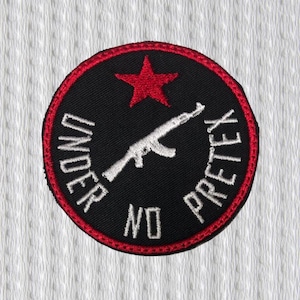 Peut inclure: Un écusson rond noir avec une bordure rouge et une étoile rouge en haut. Un fusil blanc est au centre, et les mots "UNDER NO PRETEX" sont brodés en blanc sur le bord.