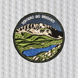 May include: Embroidered patch featuring a mountain landscape with a lake. The patch has a circular shape with the text "SENTIERO DEI BRIGANTI" in white. The design includes green hills, a blue lake, and snow-capped mountains.