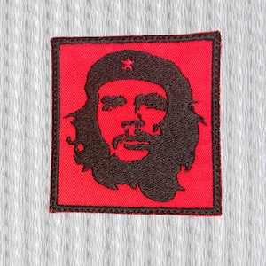 Könnte beinhalten: Ein quadratischer, roter Aufnäher mit einer schwarzen Silhouette eines Mannesgesichts mit Bart und Hut. Der Aufnäher hat einen schwarzen Rand und ist vor einem weißen, strukturierten Hintergrund platziert. Das Bild ist ein stilisiertes Porträt.