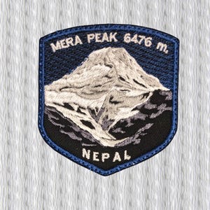 Op de afbeelding: Geborduurde patch met een berglandschap en de tekst "Mera Peak 6476 m. Nepal". De patch heeft een blauwe rand en een gedetailleerde afbeelding van een besneeuwde berg.