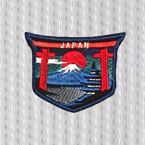 Puede incluir: Parche bordado con un paisaje japonés. El diseño incluye el Monte Fuji, un sol rojo y un torii. La palabra "JAPAN" está bordada en la parte superior. El parche tiene un borde azul marino.