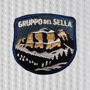 Pode incluir: Patch bordado com uma paisagem de montanha e o texto "GRUPPO DEL SELLA" em branco. O patch tem uma borda azul e retrata uma cordilheira com neve e formações rochosas douradas.