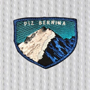 以下が含まれることがあります： 白い文字で「PIZ BERNINA」と書かれた山の風景が刺繍されたパッチ。 パッチは青い縁取りと盾の形をしています。 山は白と黒の陰影で描かれています。