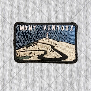 May include: A rectangular embroidered patch featuring a landscape of Mont Ventoux with a winding road leading to a summit tower. The design includes a blue sky, beige mountain terrain, and a black border. The text MONT VENTOUX is stitched in white.